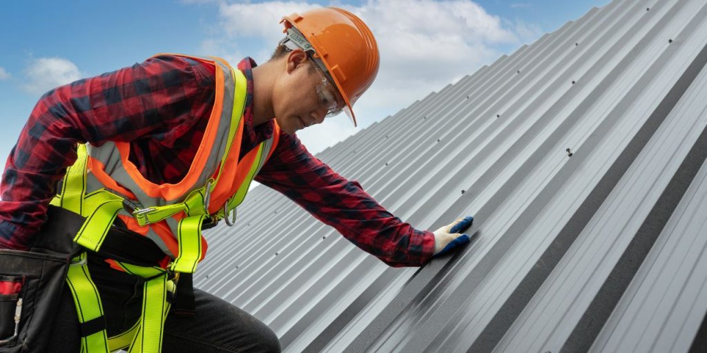 Construction worker in safety gear inspecting a metal roof.