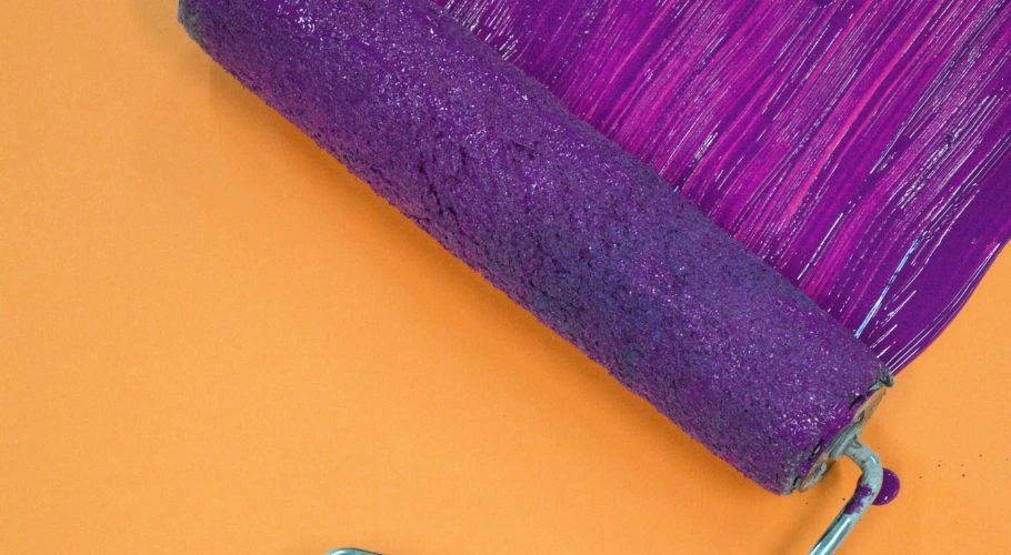 A paint roller with purple paint.