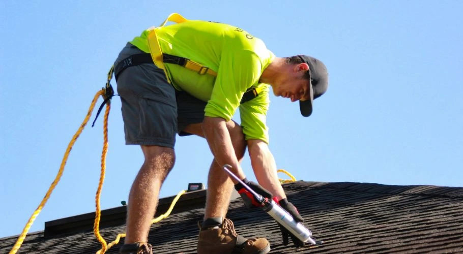 Man on the roof wearing a full-body harness with a fall arrest system.